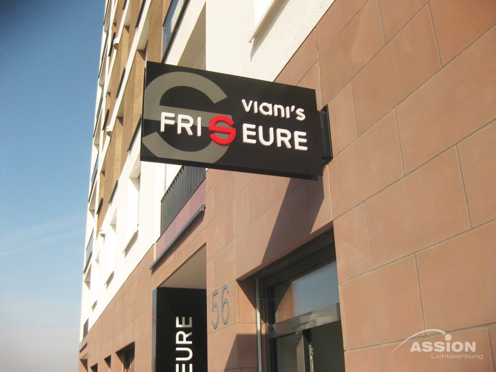 Ausleger (1) XXX Auf einem schwarz-weißen Schild an einem Gebäude steht "Viani's Friseure" mit einem roten "S"; darunter ist ein Teil der Hausnummer 56 zu sehen.
