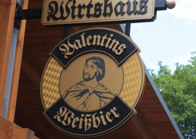 Auf einem traditionellen deutschen Wirtshausschild steht "Wirtshaus Valentins Weißbier" mit der Abbildung eines Mannes in historischer Kleidung.