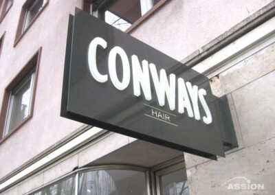 Ein rechteckiges Schild für "CONWAYS HAIR" ist an der Außenseite eines Gebäudes in der Nähe mehrerer Fenster angebracht.
