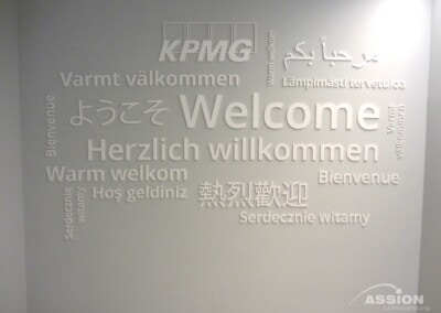 Wand mit dem Wort "Welcome" und seinen Übersetzungen in mehreren Sprachen, zusammen mit dem KPMG-Logo am oberen Rand.