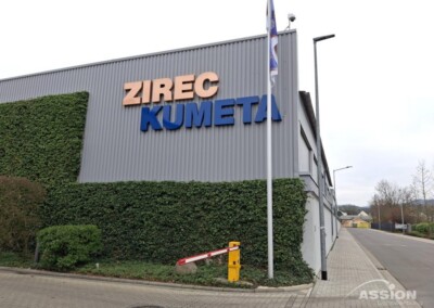 Ein Geschäftshaus mit großem Schild "ZIREC KUMETA", Efeu an der Wand und einem rot-weißen Schrankenbaum am Eingang.
