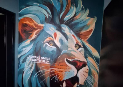 Ein farbenfrohes Wandgemälde eines Löwenkopfes mit dem Text "ALWAYS SMILE BEAUTIFULLY" (Immer schön lächeln) an einer Wand in einem schwach beleuchteten Raum.