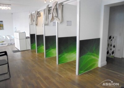 Eine Reihe von drei abgetrennten Kabinen mit grüner Verkleidung und Vorhängen in einem modernen, sauberen Innenraum mit Holzböden und weißen Wänden.