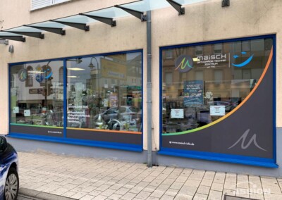 Schaufenster des "Maisch Orthopädie Technik Zentrums" mit großen Schaufenstern und einem Logo, vom Bürgersteig aus gesehen an einem bewölkten Tag.