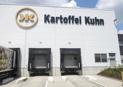 Das Äußere eines Kartoffel-Kuhn-Lagers mit drei Laderampen mit den Nummern 10, 11 und 12 und einem teilweise sichtbaren Lkw auf der linken Seite.