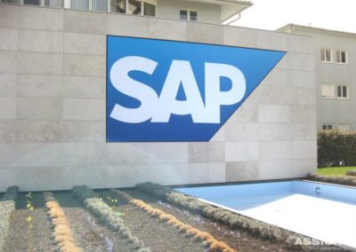 Großes SAP-Logo an der Außenwand eines modernen Gebäudes, mit Grünpflanzen und einem leeren Wasserspiel im Vordergrund.