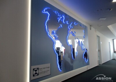 An der Wand montierte Weltkarte mit blauer LED-Beleuchtung in einem modernen Büroflur; auf der linken Seite der Wand ist ein Firmenschild zu sehen.