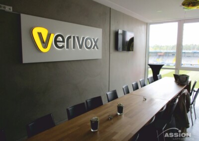 Ein moderner Konferenzraum mit einem langen Tisch, schwarzen Stühlen und einem "Verivox"-Schild an der Wand; ein Fenster gibt den Blick auf ein Stadion frei.
