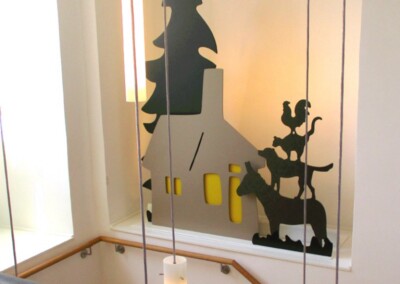 Ein dekoratives Display mit schwarzen Scherenschnitten, die ein Haus, einen Baum und gestapelte Tiere in einem Treppenhaus mit modernen Hängelampen zeigen.