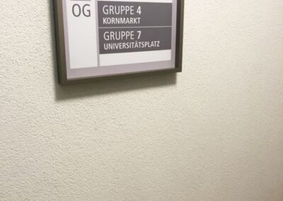Wandschild auf einer weißen Wand, das die Lage der Räume der "Gruppe 4 Kornmarkt" und der "Gruppe 7 Universitätsplatz" im 2. Stock der Südstadtresidenz Caroline Sammet anzeigt.