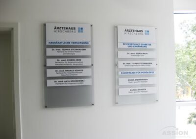 Im Ärztehaus Hirschberg, einem medizinischen Zentrum, sind auf zwei weißen Wandtafeln neben einem Fenster die Namen und Fachgebiete der Ärzte aufgeführt.