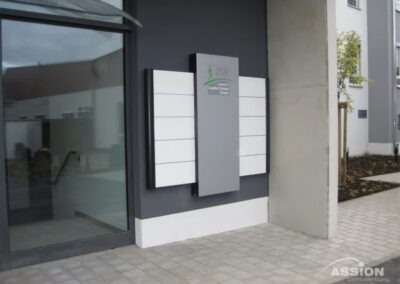 Ein moderner Gebäudeeingang mit einem an der Wand montierten Schild mit dem Logo und dem Namen einer Organisation, umgeben von leeren weißen Tafeln.