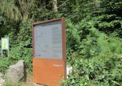 Am Rande eines Waldweges, umgeben von dichtem Grün, steht ein Hinweisschild auf den WildPark Schloss Karlsberg.