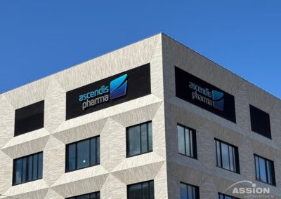 Ein modernes Bürogebäude mit "ascendis pharma"-Schildern an der oberen Fassade vor einem strahlend blauen Himmel.