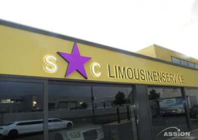 Ein Schaufenster mit einem gelben Schild mit der Aufschrift "S*C LIMOUSINENSERVICE" in Leuchtbuchstaben und einem lila Stern zwischen S und C; im Hintergrund sind Limousinen zu sehen.