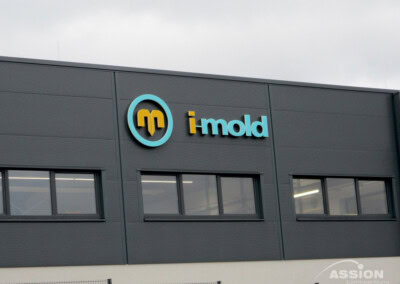 Ein modernes Industriegebäude mit dem "i-mold"-Logo und -Namen an der grauen Außenwand über mehreren Fenstern.