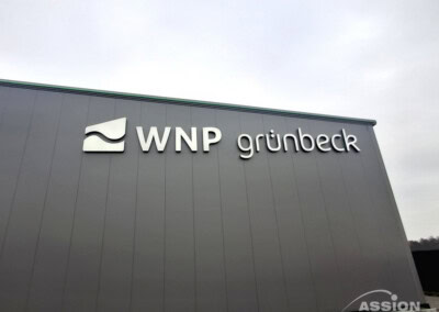 Das Äußere eines grauen Gebäudes mit dem Logo und dem Namen "WNP grünbeck" an der oberen Wand.
