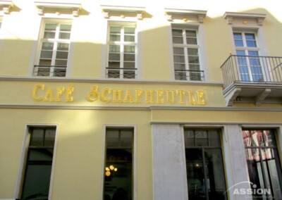 Außenansicht des Café Schafheutle, ein gelbes Gebäude mit großen Fenstern und dem Namen des Cafés in goldenen Buchstaben über dem Eingang.
