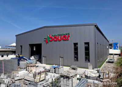 Ein großes Industriegebäude mit einem "bauer"-Schild an der Fassade, umgeben von Stapeln von Baumaterialien und Geräten.