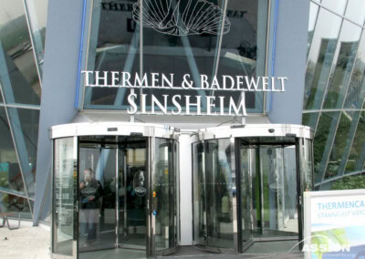 Haupteingang mit Drehtüren zur Thermen & Badewelt Sinsheim, mit Schildern über den Türen und Glasscheiben im Hintergrund.