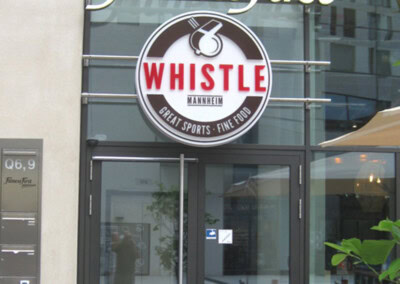 Gläserner Eingang zu einem Fitness First-Fitnessstudio mit einem großen Whistle-Sportbar- und Restaurantschild über den Türen.