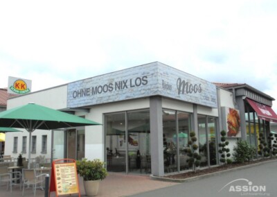 Ein Restaurant mit Sitzplätzen im Freien und einem großen Schild mit der Aufschrift "OHNE MOOS NIX LOS" an der Fassade des Gebäudes.