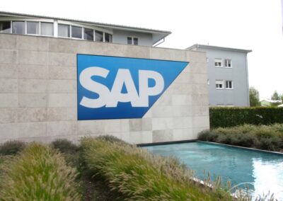 Das Äußere eines modernen Gebäudes zeigt ein großes SAP-Logo auf einer Steinmauer, mit einem kleinen Pool und Landschaftspflanzen im Vordergrund.