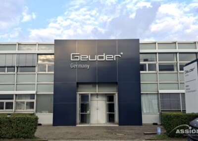 Außenansicht des Gebäudes von Geuder Germany mit Glasfenstern, einem zentralen Eingang und einem Schild mit dem Namen des Unternehmens.
