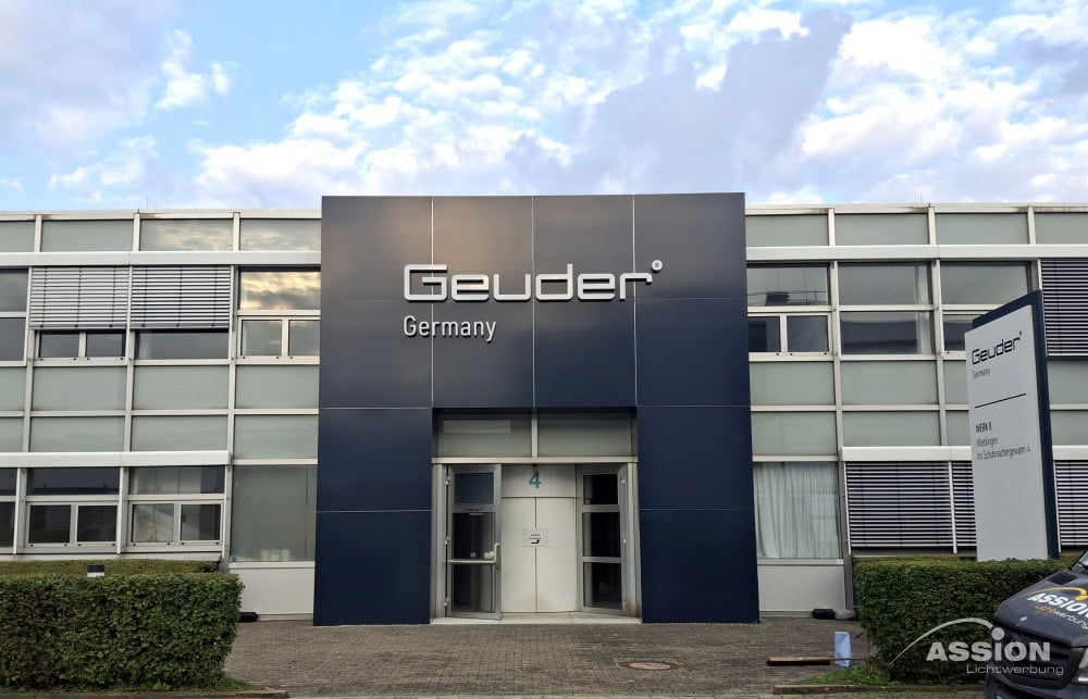 Portale (1) XXX Außenansicht des Gebäudes von Geuder Germany mit Glasfenstern, einem zentralen Eingang und einem Schild mit dem Namen des Unternehmens.