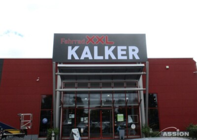 Der Eingang von Fahrrad XXL Kalker, einem Fahrradgeschäft mit einem großen Schild über den Türen an einem roten Gebäude.