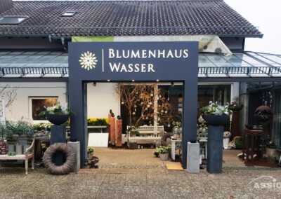 Außenansicht des Blumenhauses Wasser, eines Blumenladens mit Pflanzgefäßen im Freien und verschiedenen Pflanzen in der Nähe des Eingangs.