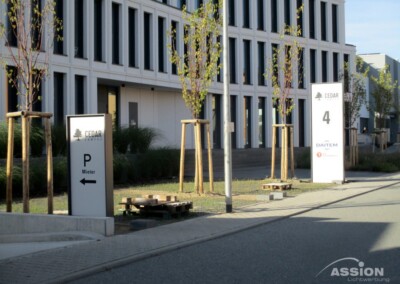 Außenbereich mit zwei Schildern mit der Aufschrift "CEDAR", eines mit dem Hinweis auf Mieterparkplätze auf der linken Seite, das andere mit der Nummer 4 vor einem modernen Bürogebäude mit jungen Bäumen.