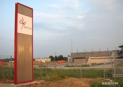 Ein großes Schild mit der Aufschrift "egomedica.at" steht in der Nähe einer eingezäunten Baustelle mit Gebäuden und einem Stadion im Hintergrund unter einem teilweise bewölkten Himmel.
