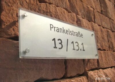 Ein Milchglasschild an einer Backsteinmauer zeigt in schwarzer Schrift die Adresse "Prankelstraße 13 / 13.1".
