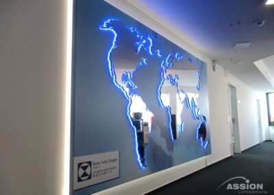 Eine Weltkarten-Wandinstallation mit blauer LED-Beleuchtung und einer Firmenplakette präsentiert Sonderanlagen in einem modernen Büroflur.