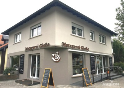 Zweistöckige Metzgerei Gieß" mit großen Fenstern, Schweinelogo und Speisekarten auf einem gepflasterten Gehweg.