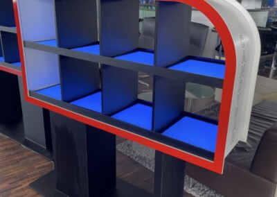 Ein schwarzes Regal mit neun quadratischen Fächern, blauer Regalbeleuchtung und einem rot-weiß geschwungenen Rand mit der Aufschrift "Herfer Electrical Consulting".