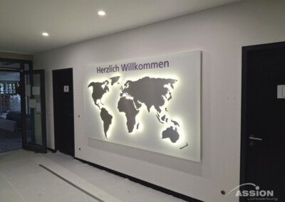 Eine beleuchtete Weltkarte mit der Aufschrift "Herzlich Willkommen" in einem modernen Flur in der Nähe mehrerer Türen.