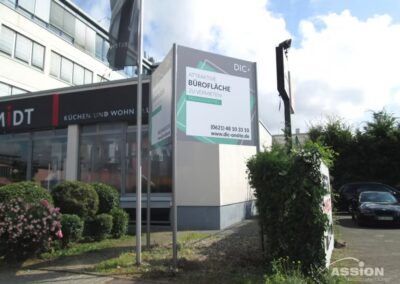 Ein Geschäftsgebäude mit einem großen Schild, das für die Vermietung von Büroräumen in deutscher Sprache wirbt, in der Nähe eines Bürgersteigs und geparkter Autos.