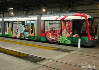 Eine moderne Straßenbahn in einem Depot ist mit einer farbenfrohen Werbung mit Bildern von Menschen, Wappen und Werbetexten beklebt.